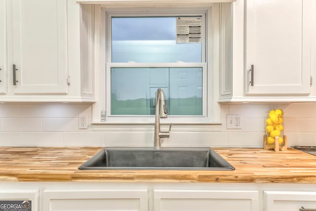 kitchen featuring a sink, wood counters, tasteful backsplash, and white cabinetry