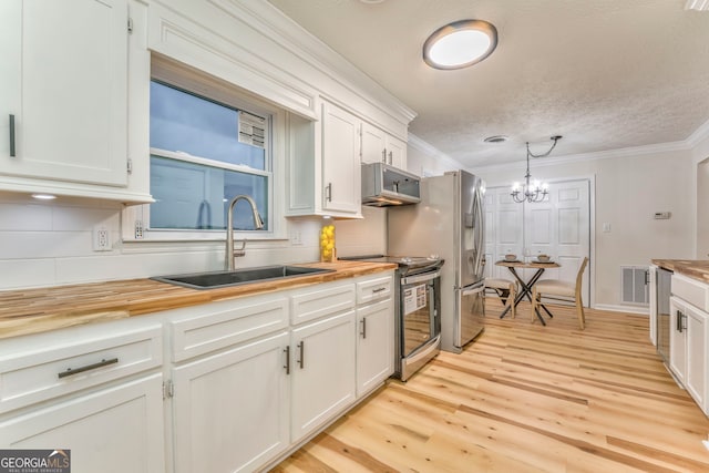 kitchen with a sink, appliances with stainless steel finishes, butcher block counters, and crown molding