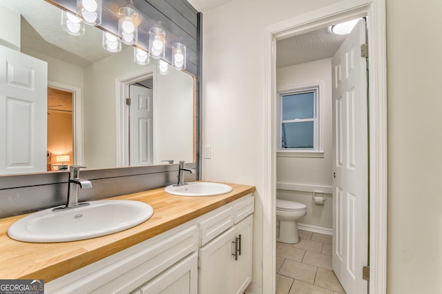 full bath with a textured ceiling, tile patterned floors, toilet, and a sink