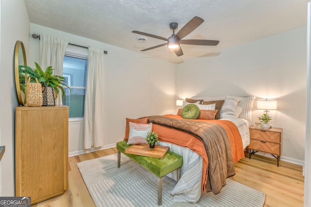 bedroom with ceiling fan, light wood-style floors, baseboards, and a textured ceiling