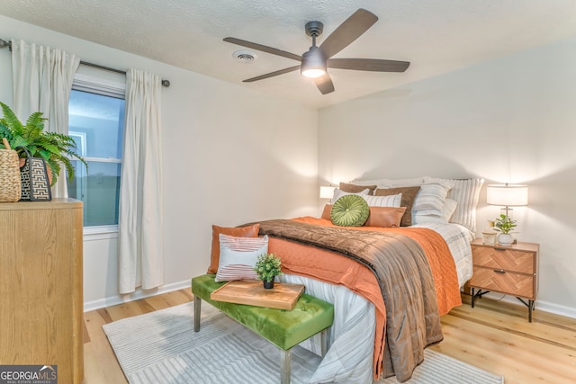 bedroom with light wood finished floors, visible vents, baseboards, ceiling fan, and a textured ceiling