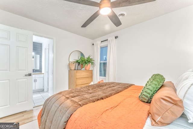 bedroom featuring visible vents, connected bathroom, a textured ceiling, and a ceiling fan