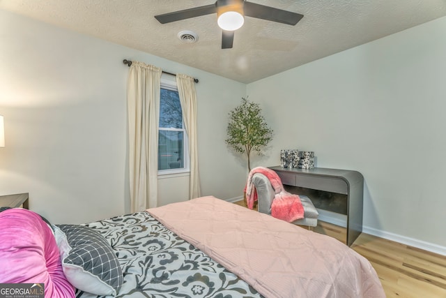 bedroom featuring a ceiling fan, visible vents, wood finished floors, baseboards, and a textured ceiling