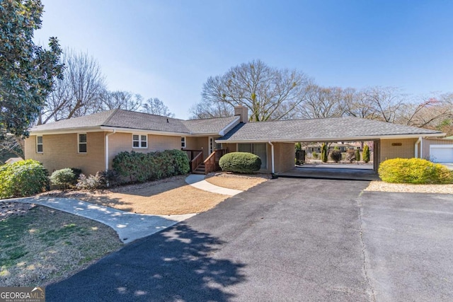 single story home featuring aphalt driveway, a chimney, brick siding, and a carport