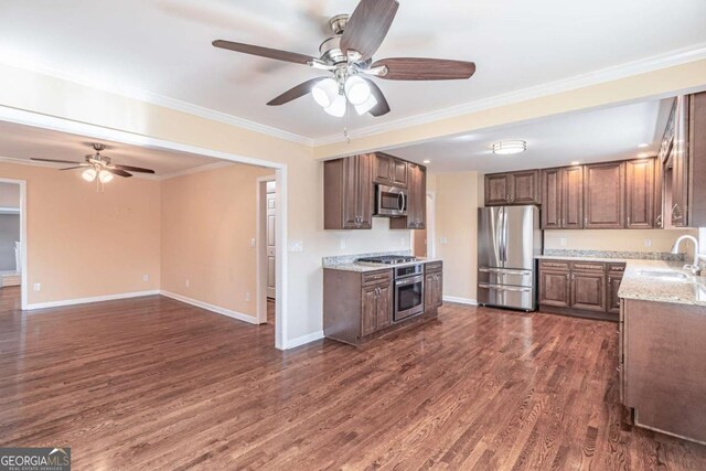 kitchen with dark wood-style floors, crown molding, appliances with stainless steel finishes, a sink, and baseboards