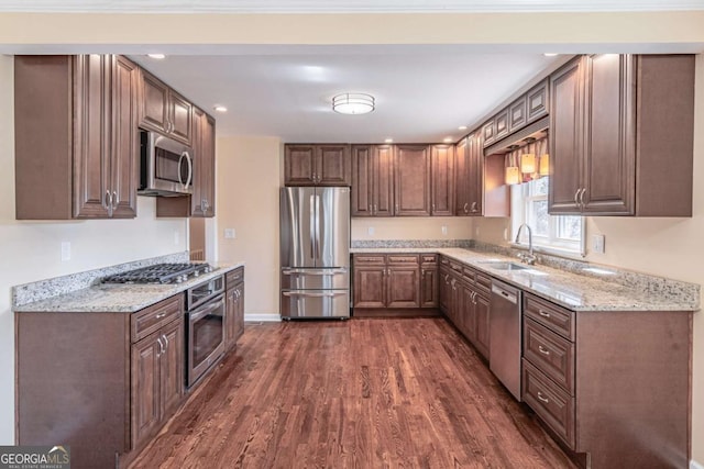 kitchen with baseboards, dark wood-type flooring, light stone countertops, stainless steel appliances, and a sink