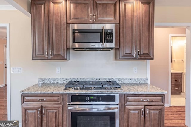 kitchen with light stone countertops, dark brown cabinets, stainless steel appliances, and wood finished floors