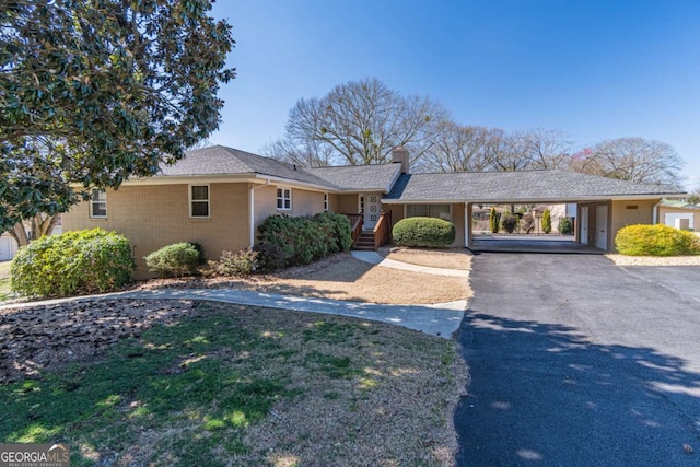 ranch-style house featuring aphalt driveway, a chimney, an attached carport, and brick siding