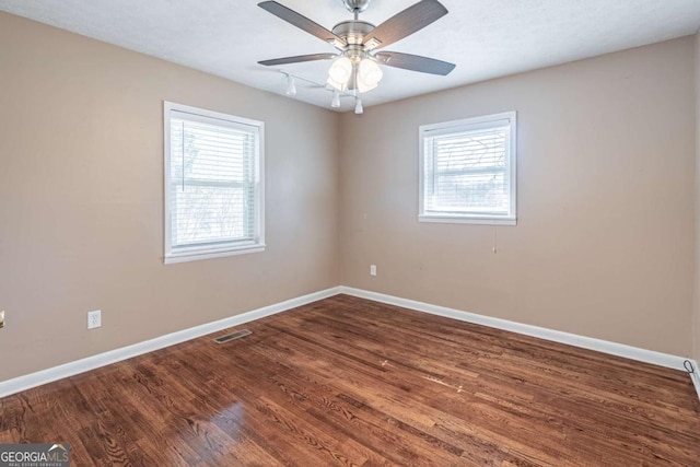 unfurnished room featuring a healthy amount of sunlight, baseboards, visible vents, and dark wood-style flooring