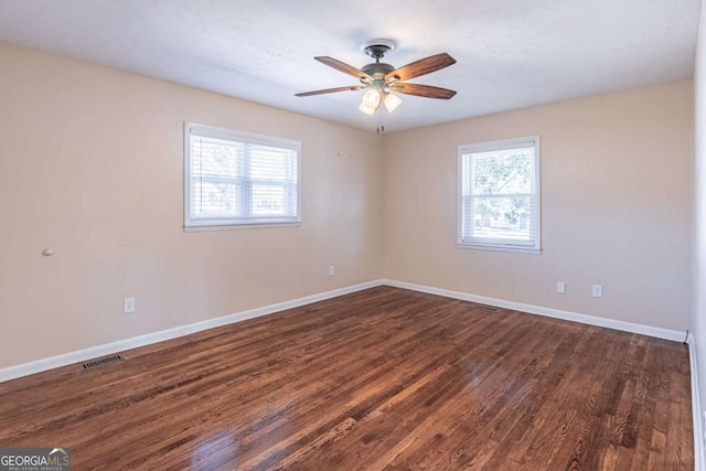 spare room featuring baseboards, visible vents, ceiling fan, and dark wood-style flooring