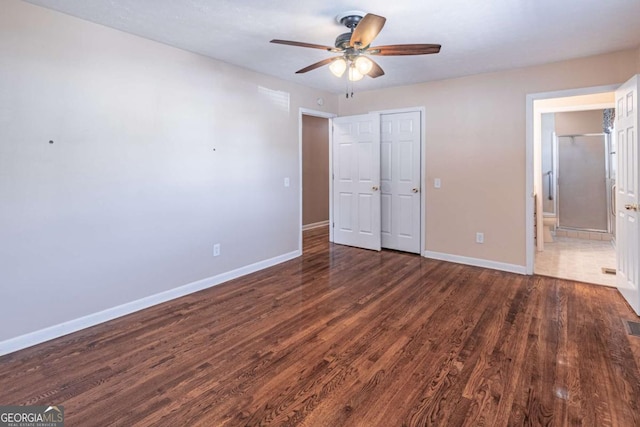 unfurnished bedroom featuring ensuite bathroom, ceiling fan, baseboards, and wood finished floors