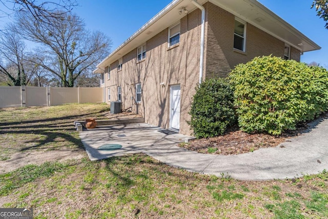 exterior space with central AC, brick siding, fence, a yard, and a patio area