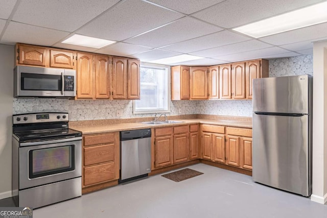 kitchen featuring appliances with stainless steel finishes, finished concrete floors, light countertops, a paneled ceiling, and a sink