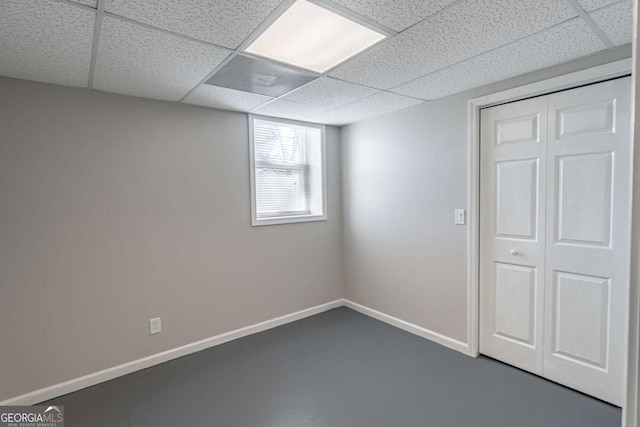 unfurnished bedroom featuring a closet, baseboards, concrete flooring, and a drop ceiling