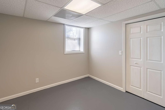 unfurnished room featuring concrete flooring, a drop ceiling, and baseboards