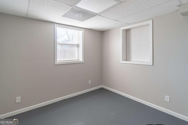 empty room with finished concrete floors, baseboards, and a drop ceiling