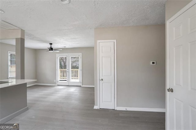 interior space with french doors, a ceiling fan, a textured ceiling, wood finished floors, and baseboards