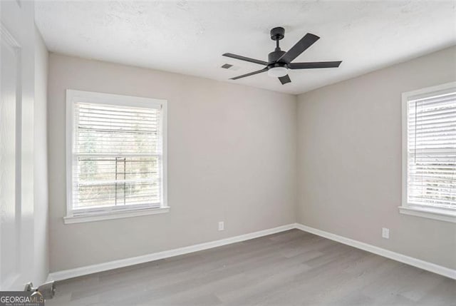 spare room featuring a ceiling fan, visible vents, baseboards, and wood finished floors