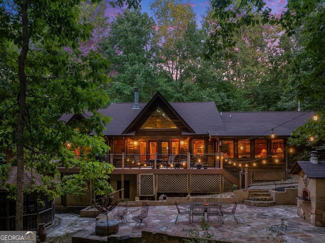 back of house at dusk featuring a patio area, roof with shingles, stairs, and a wooden deck