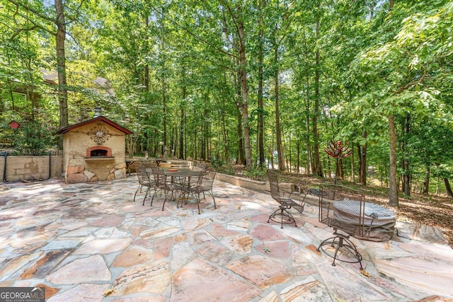 view of patio featuring outdoor dining space, an outdoor stone fireplace, and a forest view