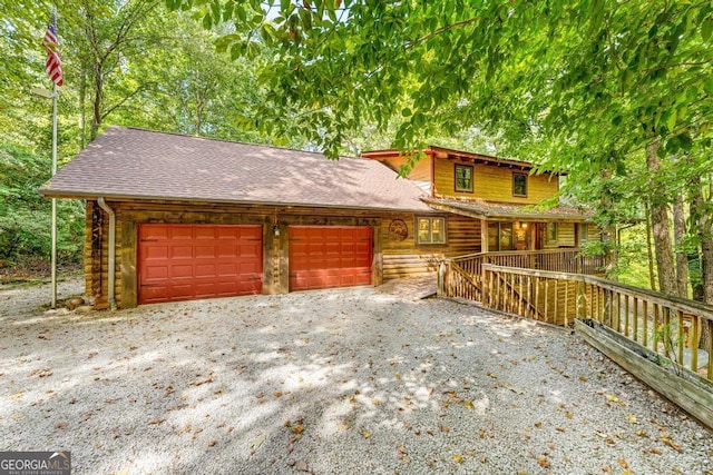 exterior space featuring a porch, a garage, roof with shingles, log siding, and gravel driveway