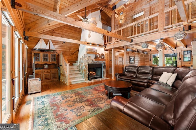 living area with ceiling fan, wooden walls, a fireplace, wood ceiling, and light wood-type flooring