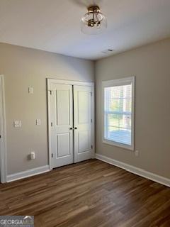 unfurnished bedroom featuring dark wood-style floors, baseboards, and a closet