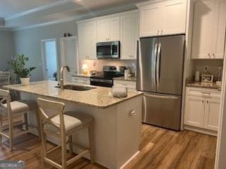 kitchen featuring stainless steel appliances, crown molding, a sink, and wood finished floors