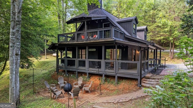 back of house with an outdoor fire pit, a patio area, a wooded view, and a sunroom