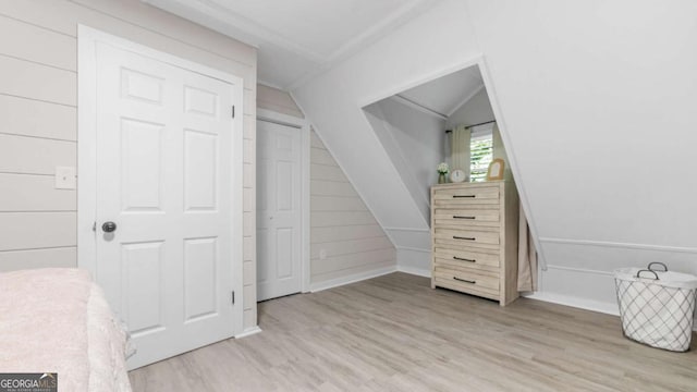 bedroom featuring vaulted ceiling, light wood-style flooring, and wooden walls