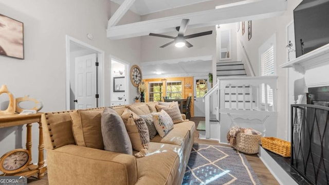 living area featuring a ceiling fan, wood finished floors, stairs, a high ceiling, and a fireplace