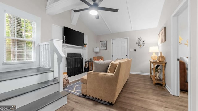 living area featuring vaulted ceiling with beams, a fireplace, a ceiling fan, wood finished floors, and baseboards