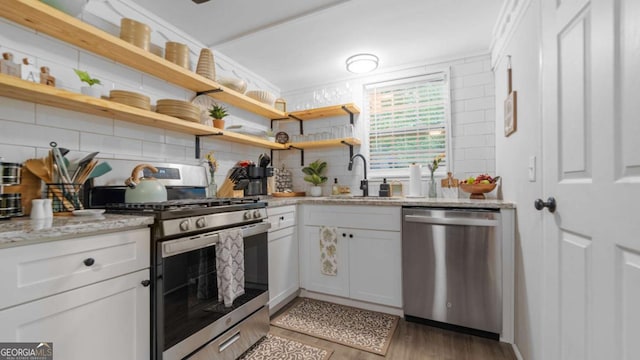 kitchen with tasteful backsplash, appliances with stainless steel finishes, light stone countertops, light wood-type flooring, and a sink