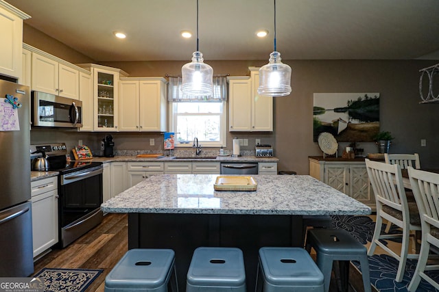 kitchen featuring dark wood-style floors, a kitchen island, a kitchen breakfast bar, stainless steel appliances, and a sink