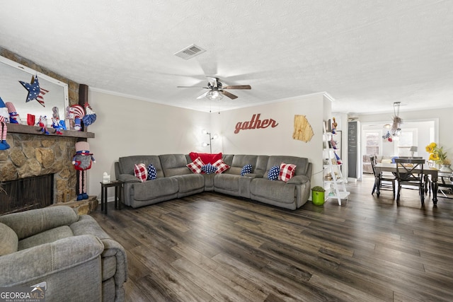 living area featuring dark wood finished floors, visible vents, ornamental molding, a stone fireplace, and a textured ceiling