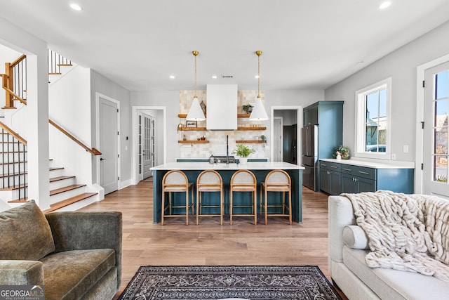 kitchen with open shelves, open floor plan, freestanding refrigerator, light wood-style floors, and a breakfast bar area