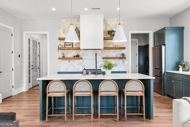 kitchen with visible vents, light countertops, an island with sink, appliances with stainless steel finishes, and open shelves