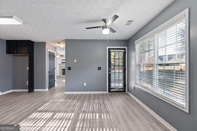 interior space with light wood finished floors, visible vents, baseboards, ceiling fan, and a fireplace