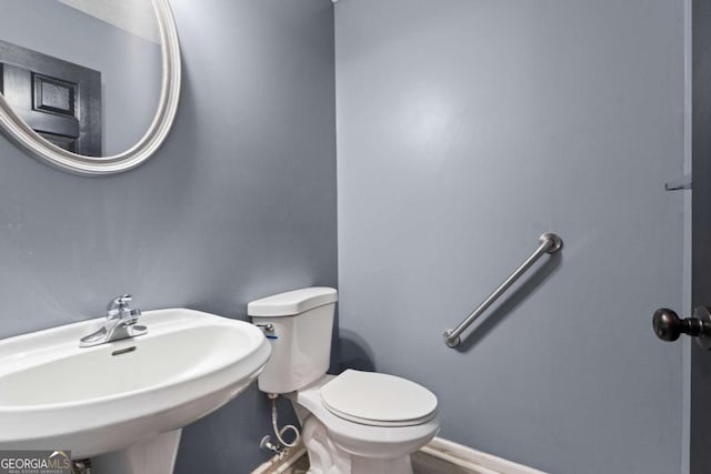 half bathroom featuring baseboards, a sink, and toilet