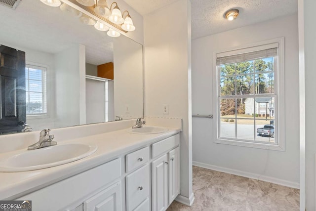 bathroom with a textured ceiling, double vanity, a sink, and visible vents