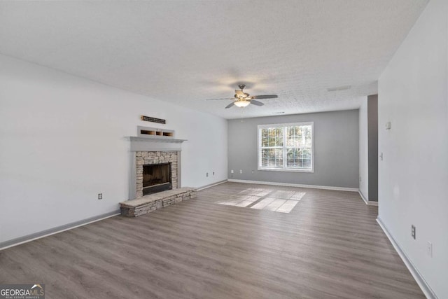 unfurnished living room featuring baseboards, a ceiling fan, wood finished floors, and a stone fireplace