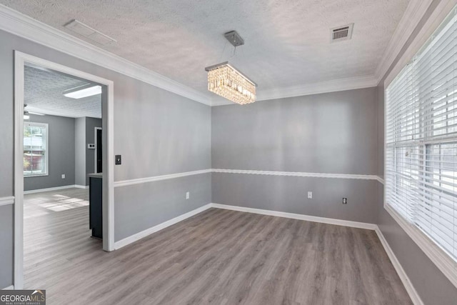 empty room featuring a textured ceiling, ornamental molding, wood finished floors, and visible vents