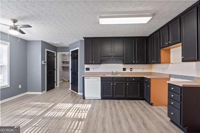 kitchen featuring a textured ceiling, white dishwasher, a sink, baseboards, and light wood finished floors