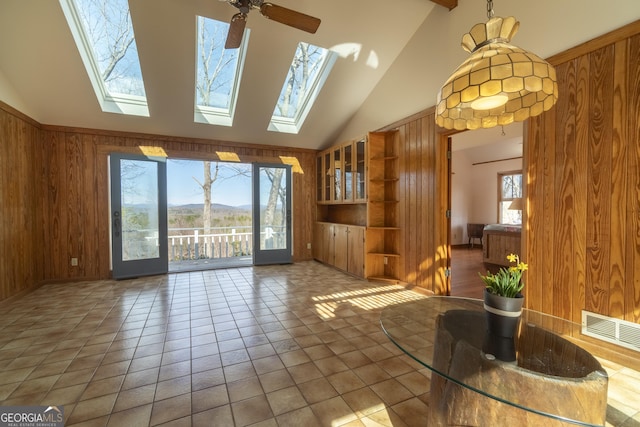 unfurnished living room featuring high vaulted ceiling, tile patterned flooring, wooden walls, a skylight, and visible vents