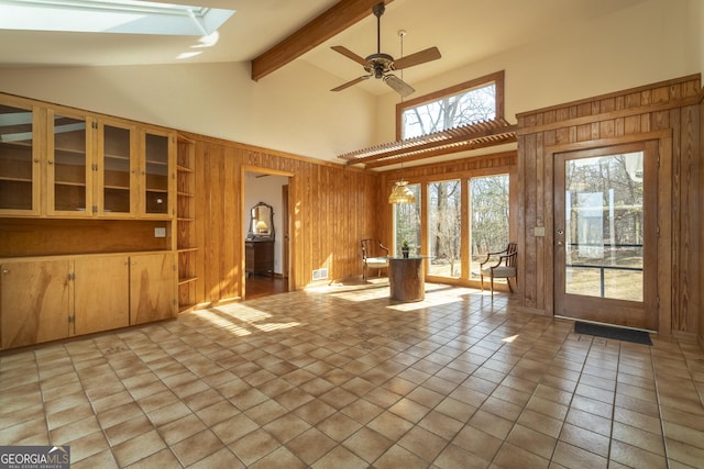 unfurnished living room featuring visible vents, ceiling fan, beamed ceiling, wood walls, and high vaulted ceiling