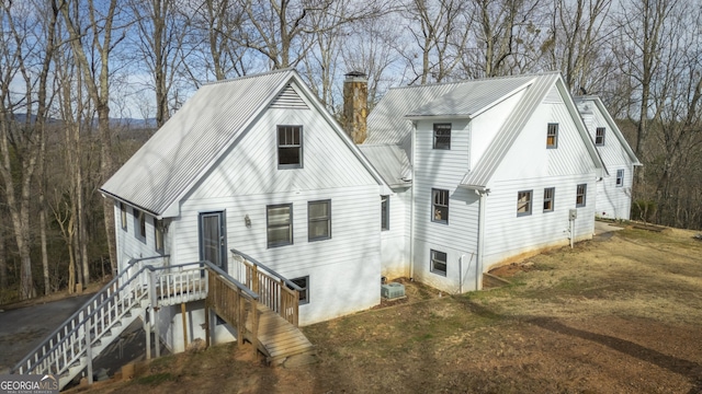 rear view of house with cooling unit, metal roof, and a chimney