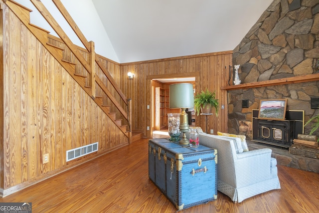 unfurnished living room featuring wooden walls, wood finished floors, visible vents, stairs, and vaulted ceiling