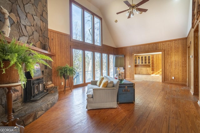 living area with a wood stove, ceiling fan, wooden walls, high vaulted ceiling, and hardwood / wood-style floors