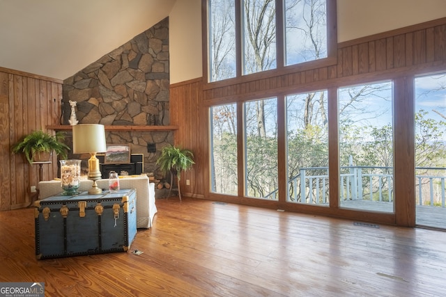 living area with wooden walls, wood finished floors, and a stone fireplace