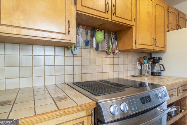 kitchen featuring tile counters, stainless steel range with electric stovetop, brown cabinetry, and tasteful backsplash